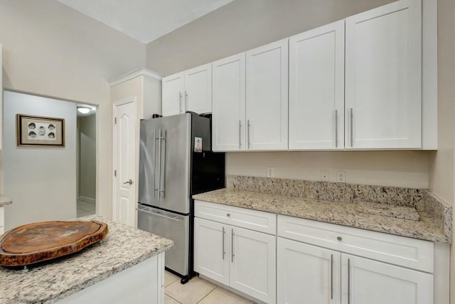 kitchen with stainless steel fridge, white cabinets, and light stone counters