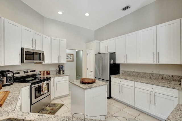 kitchen with a center island, light stone counters, light tile patterned flooring, white cabinets, and appliances with stainless steel finishes