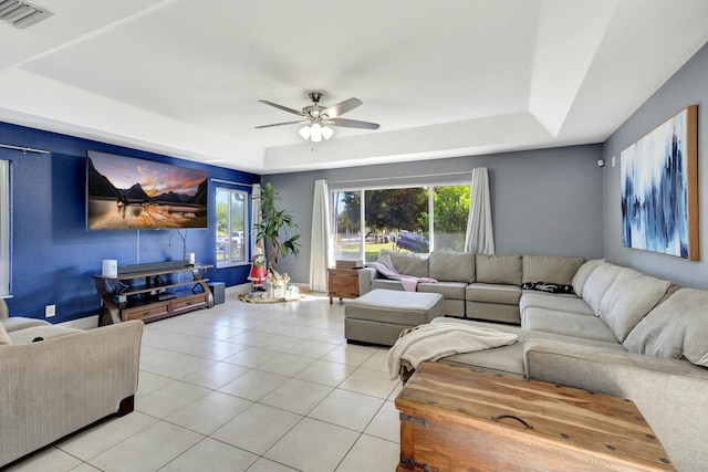 tiled living room with ceiling fan and a tray ceiling