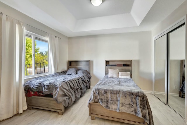 bedroom with a raised ceiling, a closet, and light hardwood / wood-style floors