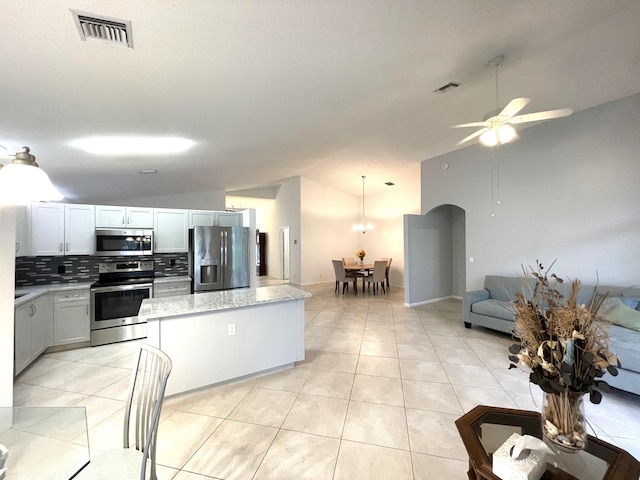 kitchen with lofted ceiling, ceiling fan, stainless steel appliances, a center island, and tasteful backsplash