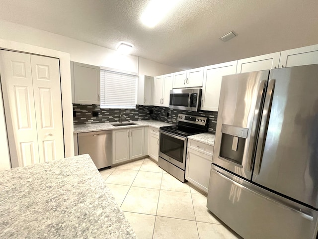 kitchen featuring appliances with stainless steel finishes, sink, decorative backsplash, light tile patterned floors, and a textured ceiling