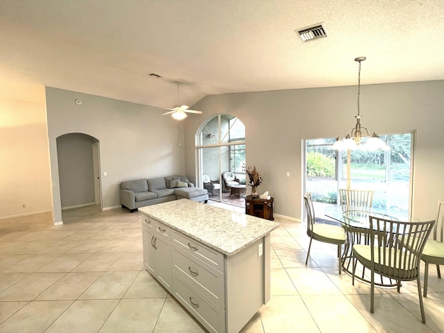 kitchen with light tile patterned flooring, a kitchen island, decorative light fixtures, lofted ceiling, and light stone countertops