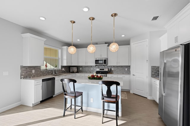 kitchen with sink, stainless steel appliances, a kitchen island, light hardwood / wood-style floors, and white cabinets