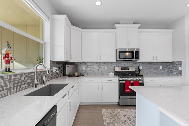 kitchen with decorative backsplash, appliances with stainless steel finishes, light stone counters, sink, and white cabinets