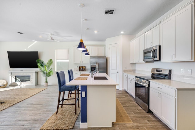 kitchen with decorative light fixtures, white cabinetry, an island with sink, and appliances with stainless steel finishes