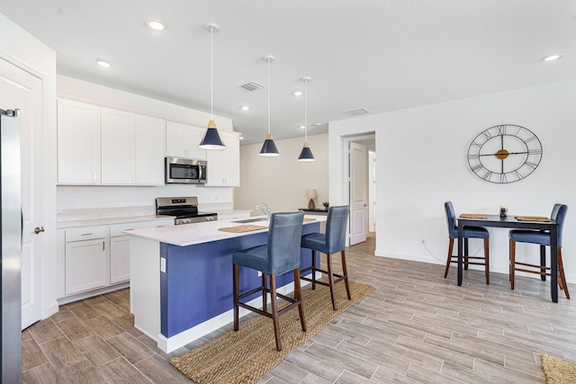 kitchen featuring appliances with stainless steel finishes, a kitchen breakfast bar, pendant lighting, a center island with sink, and white cabinetry