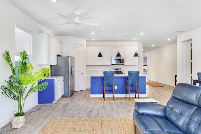 kitchen with appliances with stainless steel finishes, light hardwood / wood-style flooring, white cabinets, hanging light fixtures, and an island with sink