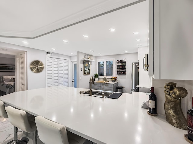 kitchen with stainless steel refrigerator, sink, kitchen peninsula, a kitchen bar, and white cabinets