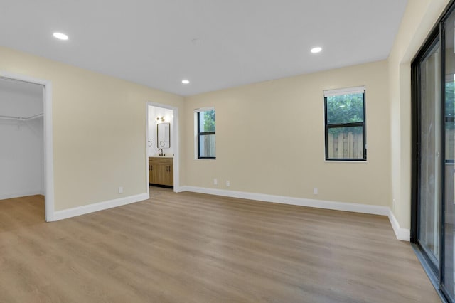 unfurnished bedroom with connected bathroom, a walk in closet, light hardwood / wood-style floors, and multiple windows