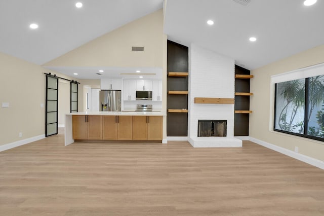 unfurnished living room featuring a barn door, light hardwood / wood-style flooring, and a brick fireplace