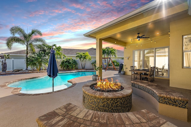 pool at dusk featuring ceiling fan, a patio, and a fire pit