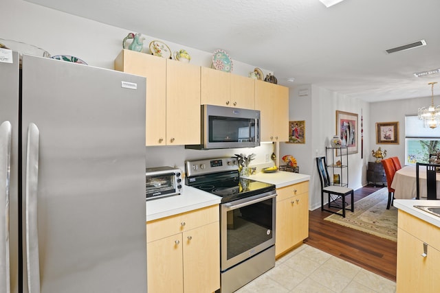 kitchen with light brown cabinetry, decorative light fixtures, appliances with stainless steel finishes, and an inviting chandelier