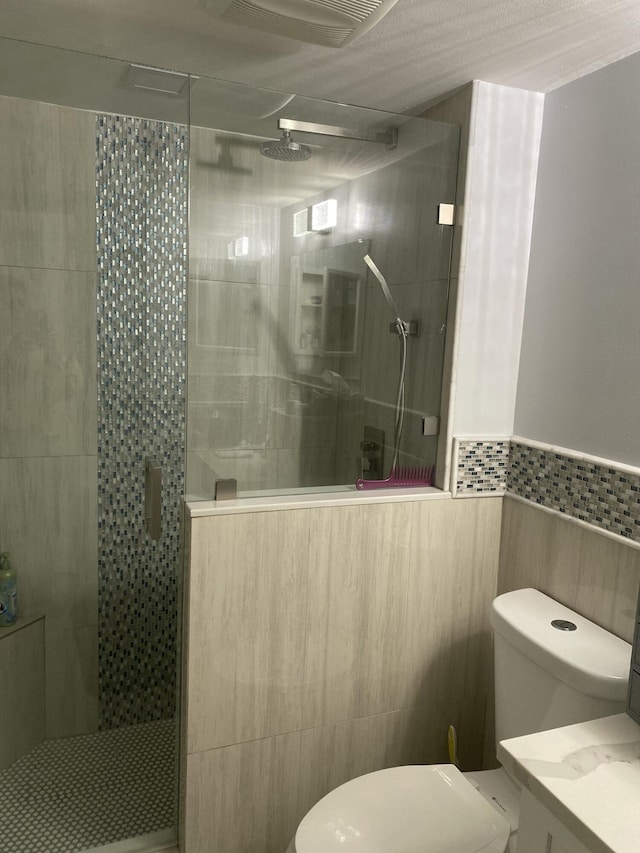 bathroom featuring a shower with door, vanity, tile walls, and toilet