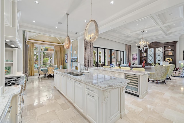 kitchen featuring coffered ceiling, sink, a center island with sink, and decorative light fixtures