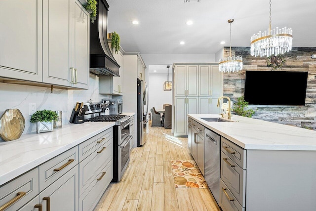 kitchen with stainless steel appliances, sink, decorative light fixtures, an inviting chandelier, and light hardwood / wood-style flooring