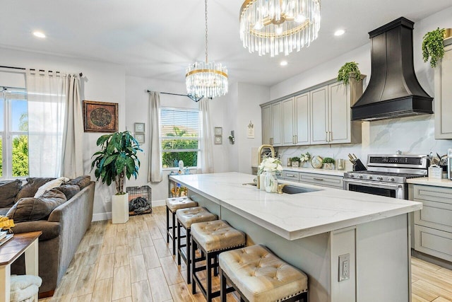 kitchen with gray cabinetry, stainless steel gas stove, an island with sink, and custom range hood