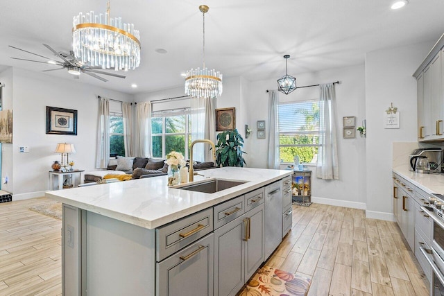 kitchen featuring sink, decorative light fixtures, gray cabinets, a center island with sink, and light wood-type flooring