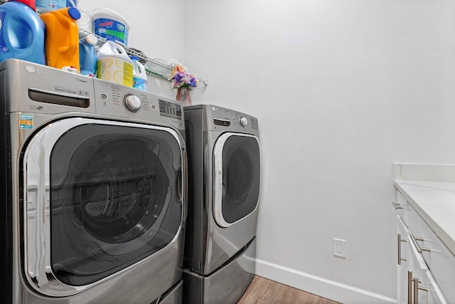 laundry area with cabinets, washing machine and dryer, and light hardwood / wood-style floors