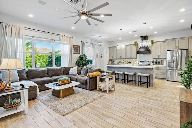 living room featuring ceiling fan with notable chandelier and light wood-type flooring