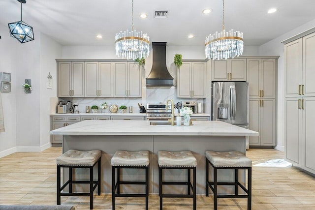 kitchen featuring a center island with sink, a kitchen breakfast bar, custom range hood, and stainless steel appliances