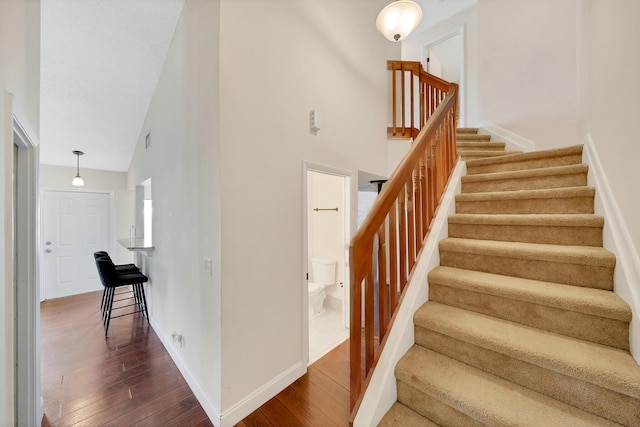 stairs with hardwood / wood-style floors and high vaulted ceiling