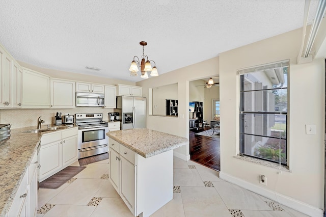 kitchen featuring a textured ceiling, stainless steel appliances, sink, a center island, and hanging light fixtures