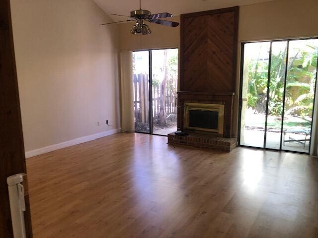 unfurnished living room with a fireplace, a high ceiling, hardwood / wood-style flooring, and ceiling fan