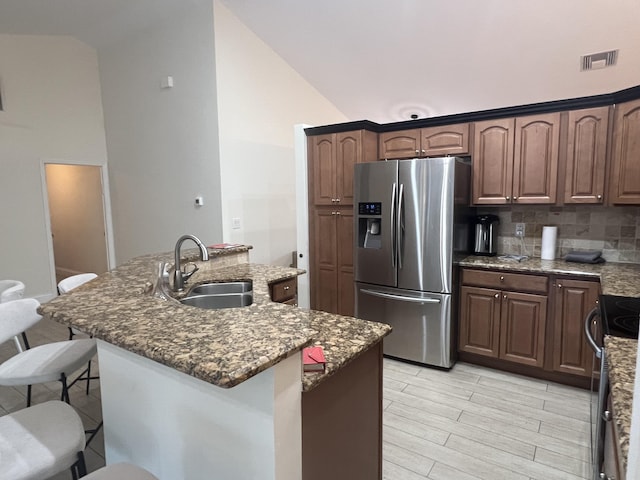 kitchen with stainless steel fridge, an island with sink, dark stone counters, and sink