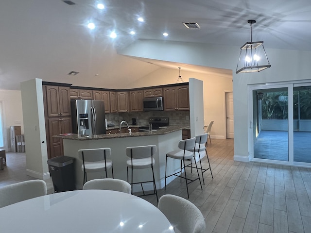 kitchen featuring a kitchen breakfast bar, dark stone countertops, light hardwood / wood-style floors, a kitchen island with sink, and appliances with stainless steel finishes