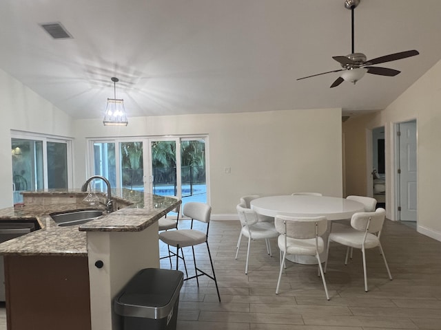 dining space with ceiling fan with notable chandelier, light hardwood / wood-style flooring, lofted ceiling, and sink