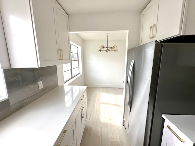 kitchen with light wood-type flooring, pendant lighting, a chandelier, white cabinetry, and stainless steel refrigerator