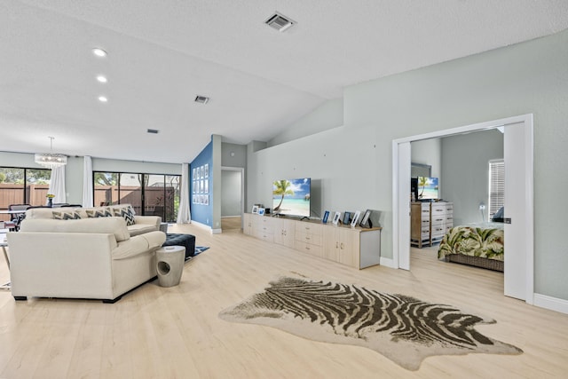 living room with a textured ceiling, a notable chandelier, lofted ceiling, and light wood-type flooring