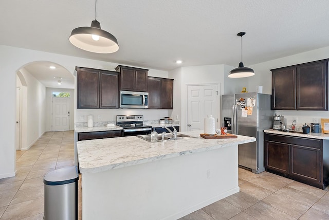 kitchen with appliances with stainless steel finishes, dark brown cabinetry, sink, a center island with sink, and hanging light fixtures