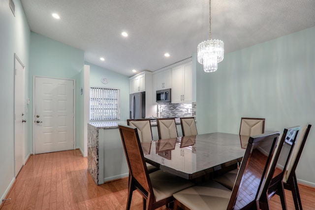 dining room with a textured ceiling, a notable chandelier, vaulted ceiling, and light wood-type flooring