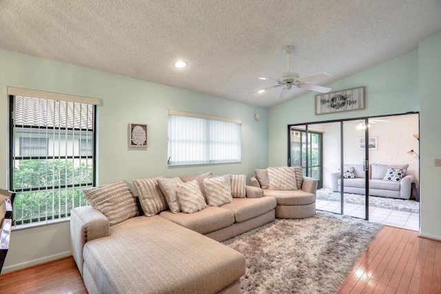 living room with a textured ceiling, light hardwood / wood-style floors, vaulted ceiling, and ceiling fan