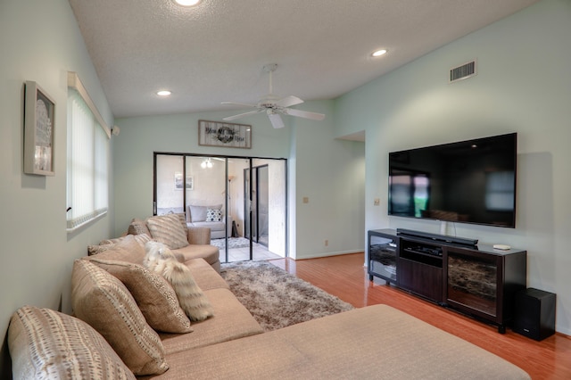 living room featuring a textured ceiling, ceiling fan, vaulted ceiling, and light wood-type flooring