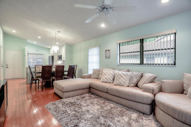 living room featuring hardwood / wood-style floors, ceiling fan with notable chandelier, a textured ceiling, and vaulted ceiling