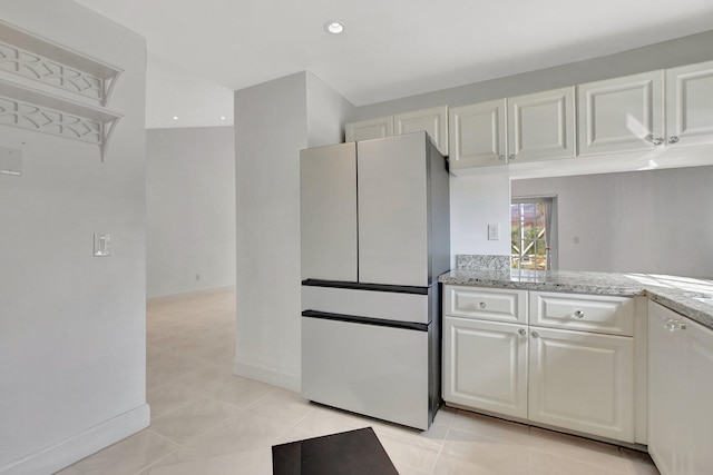 kitchen with white refrigerator, light stone counters, white cabinetry, and light tile patterned floors