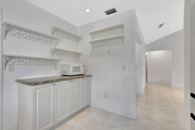 kitchen featuring white cabinets, light tile patterned floors, dark stone counters, and vaulted ceiling