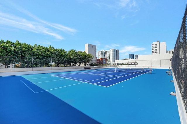 view of tennis court with a view of city and fence