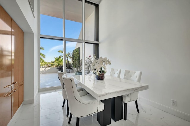 dining area featuring a high ceiling, marble finish floor, floor to ceiling windows, and baseboards