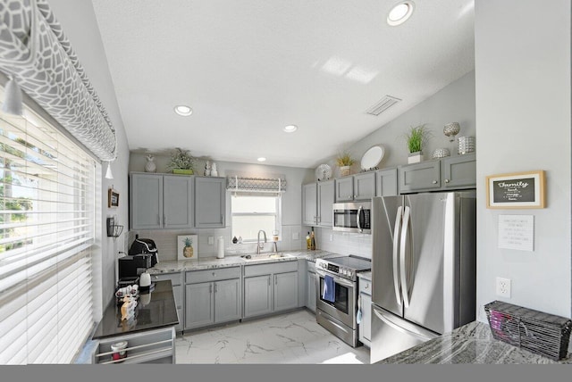 kitchen with sink, light stone counters, lofted ceiling, decorative backsplash, and appliances with stainless steel finishes