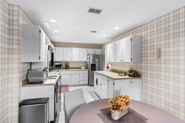 kitchen with appliances with stainless steel finishes, backsplash, light tile patterned floors, washer / clothes dryer, and white cabinetry