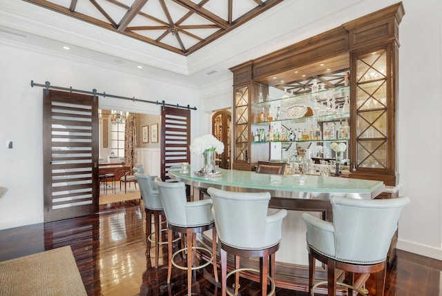 bar with a barn door, dark wood-type flooring, and crown molding