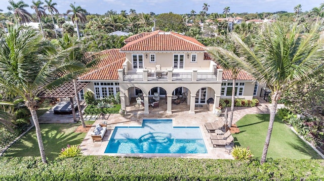 back of house featuring a lawn, a patio area, a balcony, and a pool with hot tub