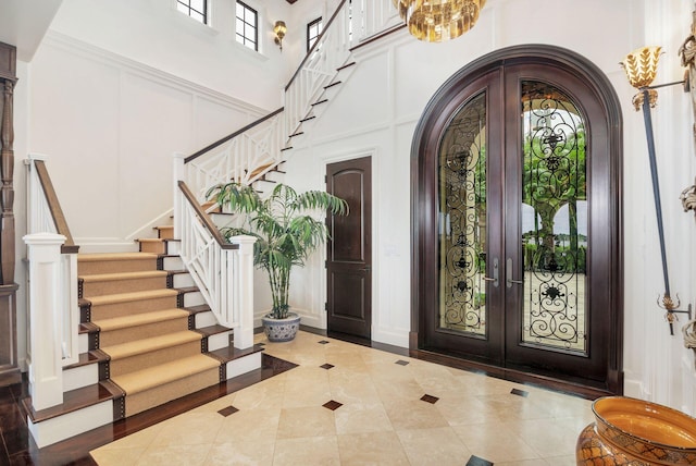 entryway featuring crown molding, french doors, a chandelier, and a high ceiling