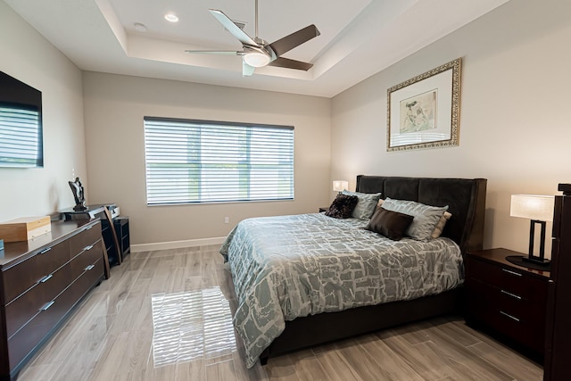 bedroom with a raised ceiling, light hardwood / wood-style flooring, and ceiling fan