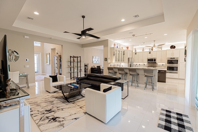 living room with light tile patterned floors, a tray ceiling, and ceiling fan