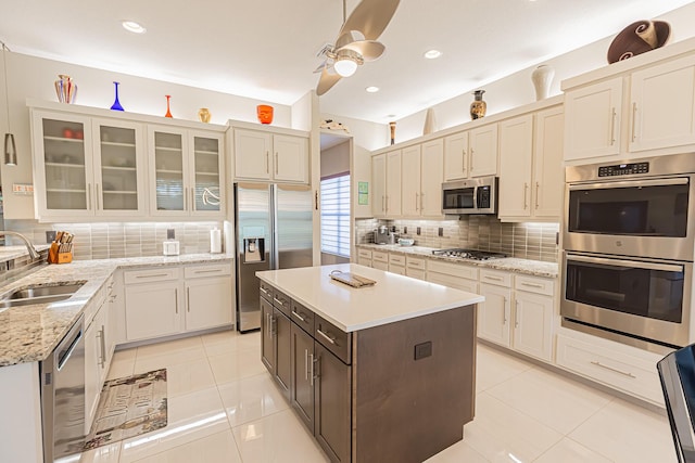 kitchen featuring backsplash, stainless steel appliances, sink, light tile patterned floors, and a center island